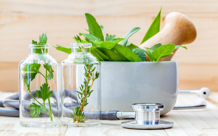 Alternative health care concept. Fresh herbs green mint ,rosemary ,parsley ,sage and lemon thyme in laboratory glassware with stethoscope on wooden background.の写真素材