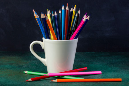 side view of a bunch of colored pencils in a white cup on dark backgroundの写真素材