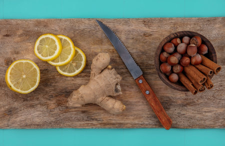 top view of ginger and lemon slices with bowl of cinnamon and nuts with knife on cutting board on blue backgroundの写真素材