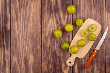 top view of whole and half cut plums on cutting board with knife on wooden background with copy spaceの写真素材