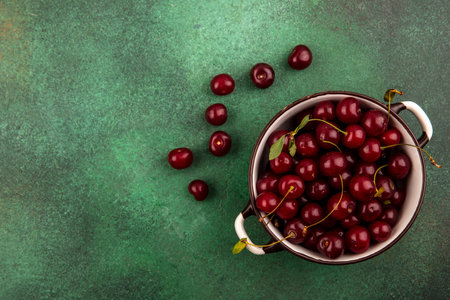 top view of cherries in bowl and on green background with copy space