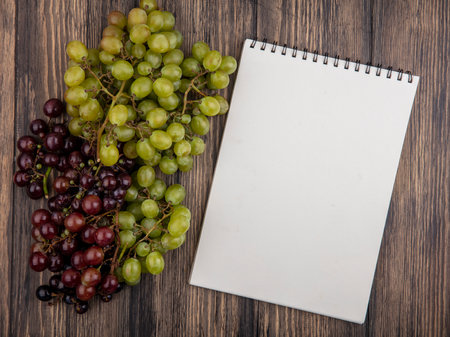 top view of black and white grapes and note pad on wooden background with copy spaceの写真素材