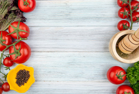 top view of vegetables as tomato coriander with black pepper garlic crusher on left and right sides and wooden background with copy spaceの写真素材