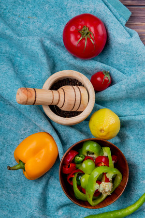 top view of vegetables as whole and sliced peppers and tomatoes with lemon and black pepper in garlic crusher on blue cloth backgroundの写真素材