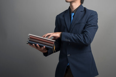 Close up of businessman in blue suit holding books on gray background