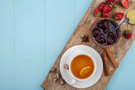 top view of strawberry jam on a wooden kitchen board with a cup of tea with cinnamon sticks on a blue background with copy spaceの写真素材