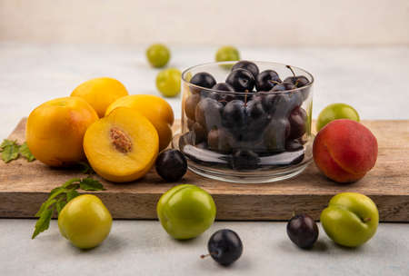 side view of fresh yellow peaches on a wooden kitchen board with dark purple sloes on a glass bowl...