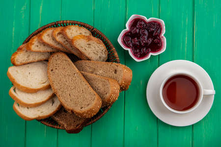 top view of breads as seeded brown cob and baguette slices in basket and raspberry jam in bowl with...