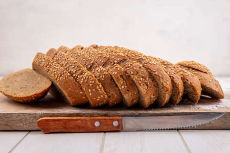 side view of sliced brown seeded cob on cutting board and knife on wooden surface and white...