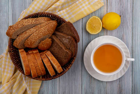 top view of breads as sliced seeded brown cob rye and crusty ones in basket on plaid cloth and cup of hot toddy with half cut lemon on wooden backgroundの写真素材