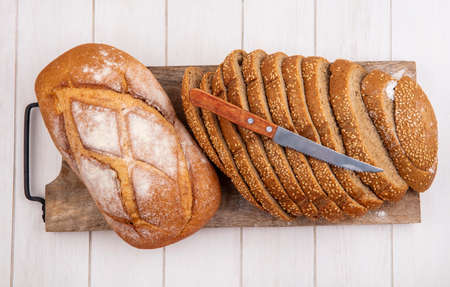 top view of breads as sliced brown seeded cob and crusty bread with knife on cutting board on wooden...