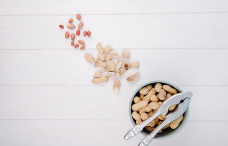 top view of peanuts in a bowl with nut cracker on white backgroundの写真素材