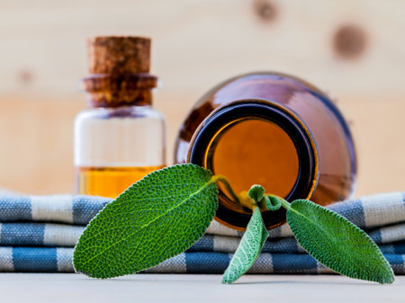 Bottle of essential oil with fresh sage leaves shallow depth of field on old wooden background.の写真素材