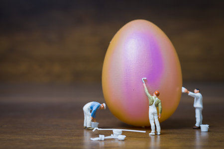 Miniature people :Painter is painting Easter-eggs for Easter day on wooden background