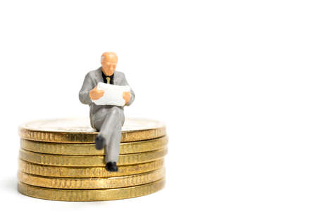 Miniature people: Businessman sitting on stack of coinの写真素材