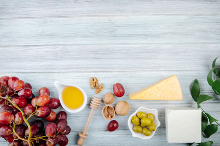 top view of pieces of cheese with honey, fresh grape, pickled olives and walnuts on grey wooden background with copy spaceの写真素材
