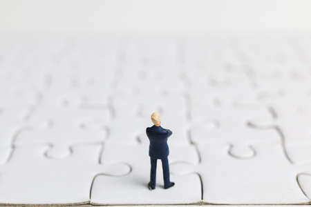 Miniature people: Businessman standing on white jigsaw.