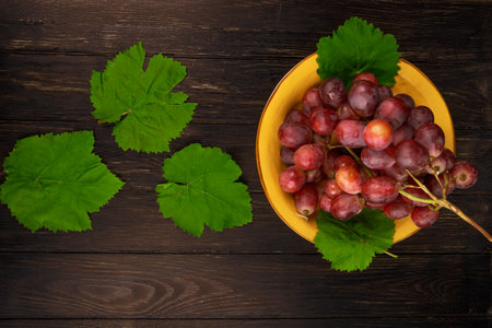 top view of fresh sweet grape in a plate and green grape leaves on dark wooden backgroundの写真素材