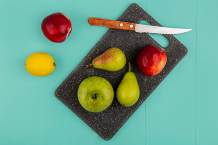 top view of fruits as pear peach apple with knife on cutting board and lemon on blue backgroundの写真素材