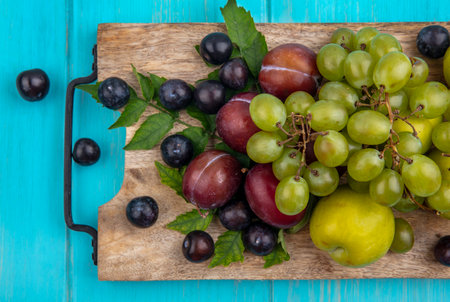 top view of fruits as grapes pluots with grape berries and leaves on cutting board on blue backgroundの写真素材