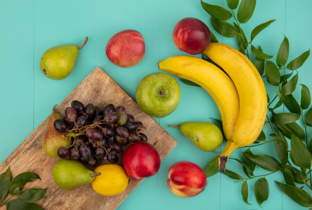 top view of fruits as peach pear lemon grape on cutting board with apple banana and leaves on blue backgroundの写真素材