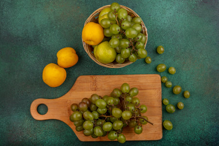 top view of fruits as bunch of grape on cutting board and nectacot pluot and grape in basket with grape berries on green backgroundの写真素材