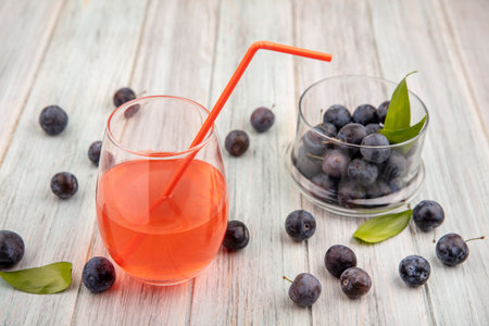 top view of the small sour blue-black sloes on a glass bowl with juice on a glass with sloes isolated on a grey wooden backgroundの写真素材