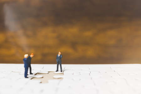 Miniature people: Businessman standing on jigsaw with wooden backgroundの写真素材