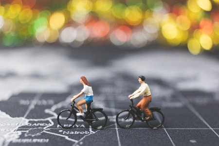 Miniature people travelers riding bicycle on world map