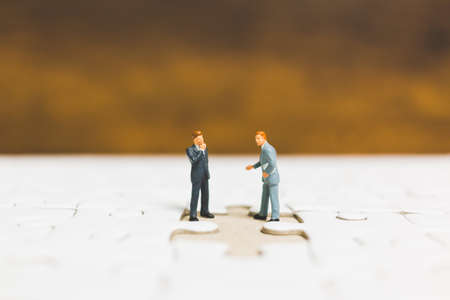 Miniature people: Businessman standing on jigsaw with wooden backgroundの写真素材