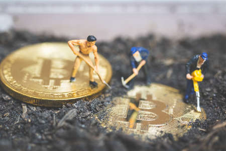 Miniature people : Worker team digging ground to uncover big shiny bitcoin