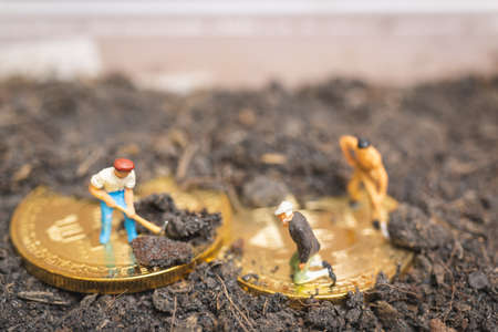 Miniature people : Worker team digging ground to uncover big shiny bitcoin