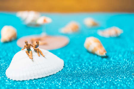 Miniature people wearing swimsuit relaxing on a seashell