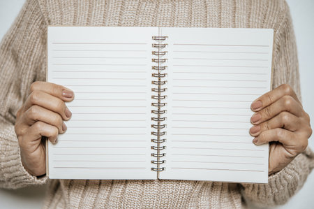 A woman who wears a long sleeve and holds a notebook open between her breasts.の写真素材