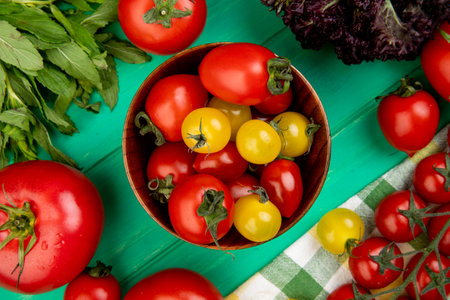 top view of tomatoes in bowl with green mint leaves and basil on green backgroundの写真素材