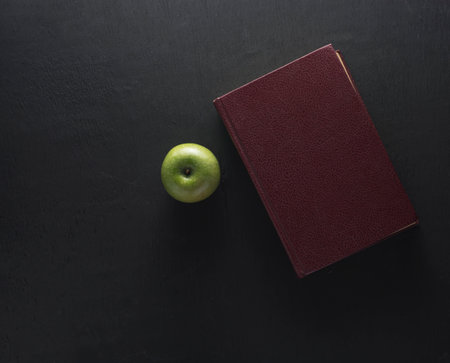 Top view Green apple with old book on black wood background. School conceptの写真素材