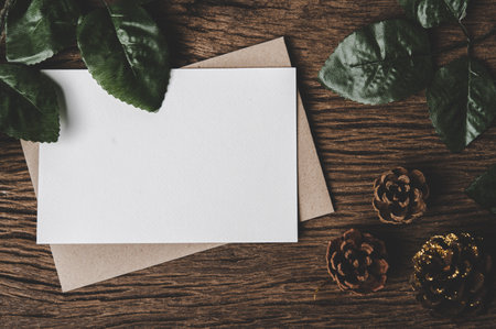 A blank card is placed on envelope and leaf with wood background