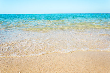 Soft waves with foam of blue ocean on the sandy beachの写真素材