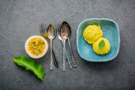 Composition of ice cream passion fruit flavor in vintage bowl setup on dark stone background . Passion fruits with pepper mint leaves and utensil.の写真素材