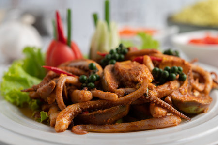 Squid fried with curry paste in white plate, with vegetables and side dishes on a white wooden...