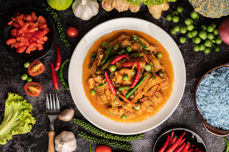 Red curry with pork in a white plate with spices on black cement.の写真素材