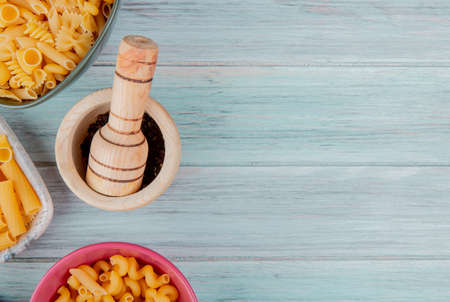 top view of different types of macaroni as ziti fusilli and others with black pepper seeds in garlic crusher on wooden background with copy spaceの写真素材