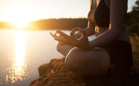 Young healthy woman is practicing yoga at mountain lake during sunset..の写真素材
