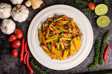 Stir fried pumpkin with minced pork in white plate, and spices on a black cement floor