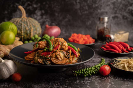 Stir-fried spicy Catfish in black plate with spices on black cement.