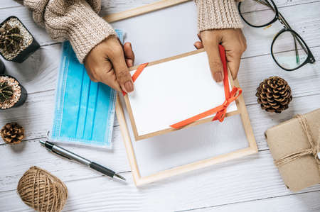 Hand holding an open card or letter, blank cover, Mock-up with a mask, glasses, pen and dried pine...