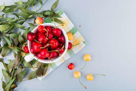 top view of cup full of red cherries on left side and white background decorated with leaves with copy spaceの写真素材