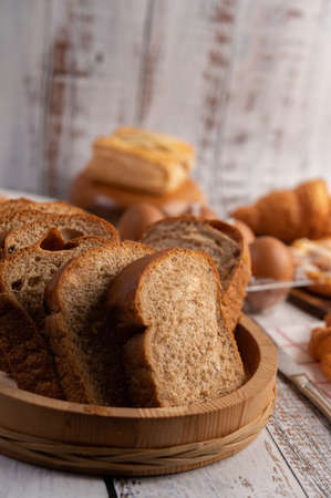 Bread slices placed in a wooden plate on a white wooden table. Selective focus.