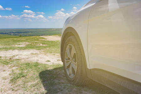 Part of the white SUV with the wheel on the background of natural landscape in the sun .