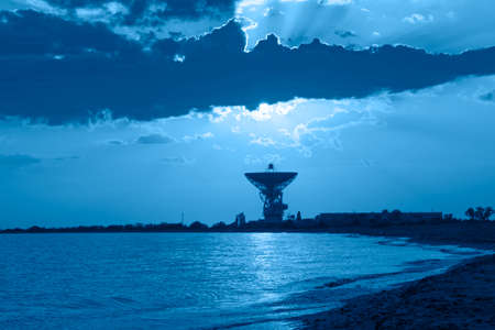 Magnificent sunset on the background of the sea and space antenna. The rays of the sunset illuminate...